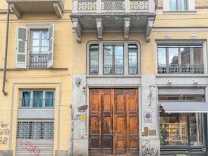 A building with a wooden door, a balcony with metal railings, and a window with a metal grate. - Mole House (Torino)