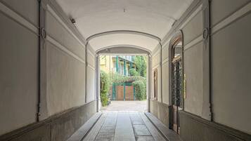 A corridor with a tiled floor, arched ceiling, and a view of a building with a green gate and steps.