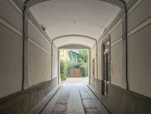 A corridor with a tiled floor, arched ceiling, and a view of a building with a green gate and steps. - Mole House (Torino)