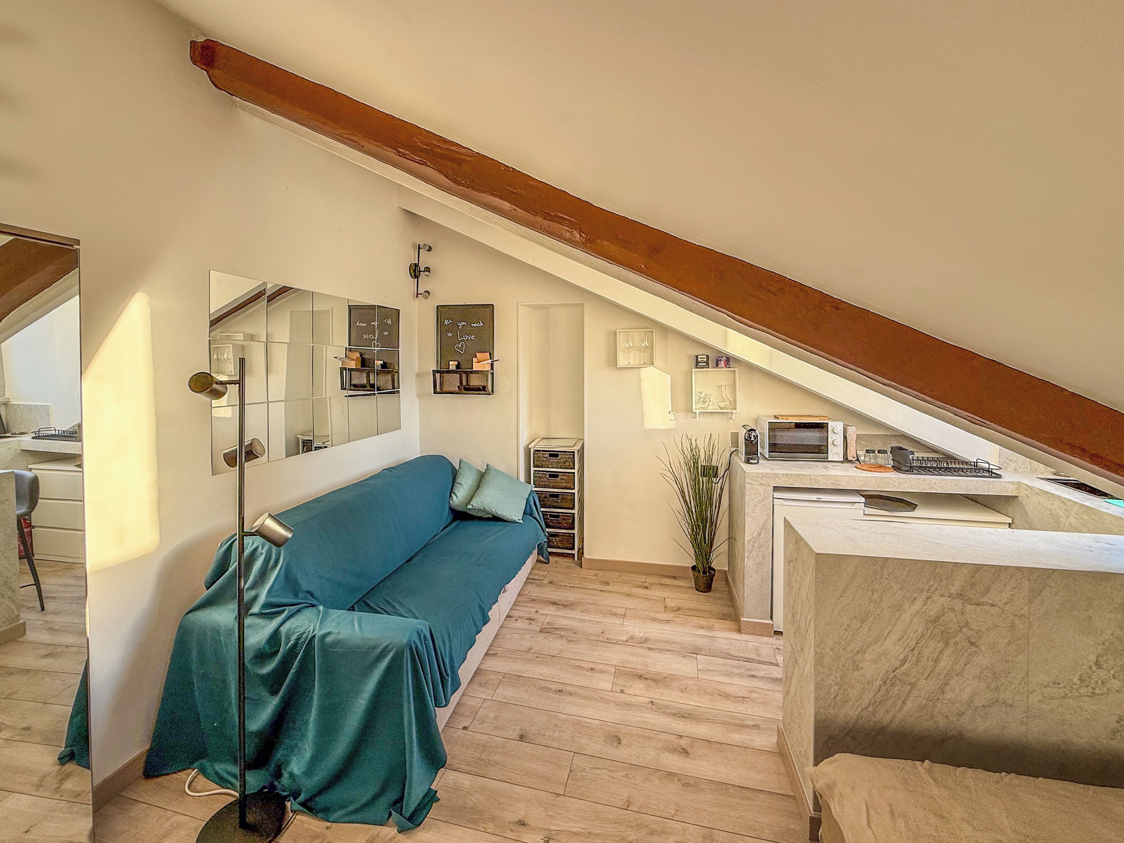 Un dormitorio estilo loft moderno con techo inclinado, un sofá azul, una pequeña kitchenette y un espejo grande.