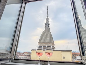 A window view of a building with a prominent tower, two glasses of red wine on the windowsill, and a clear sky. - Mole House (Torino)