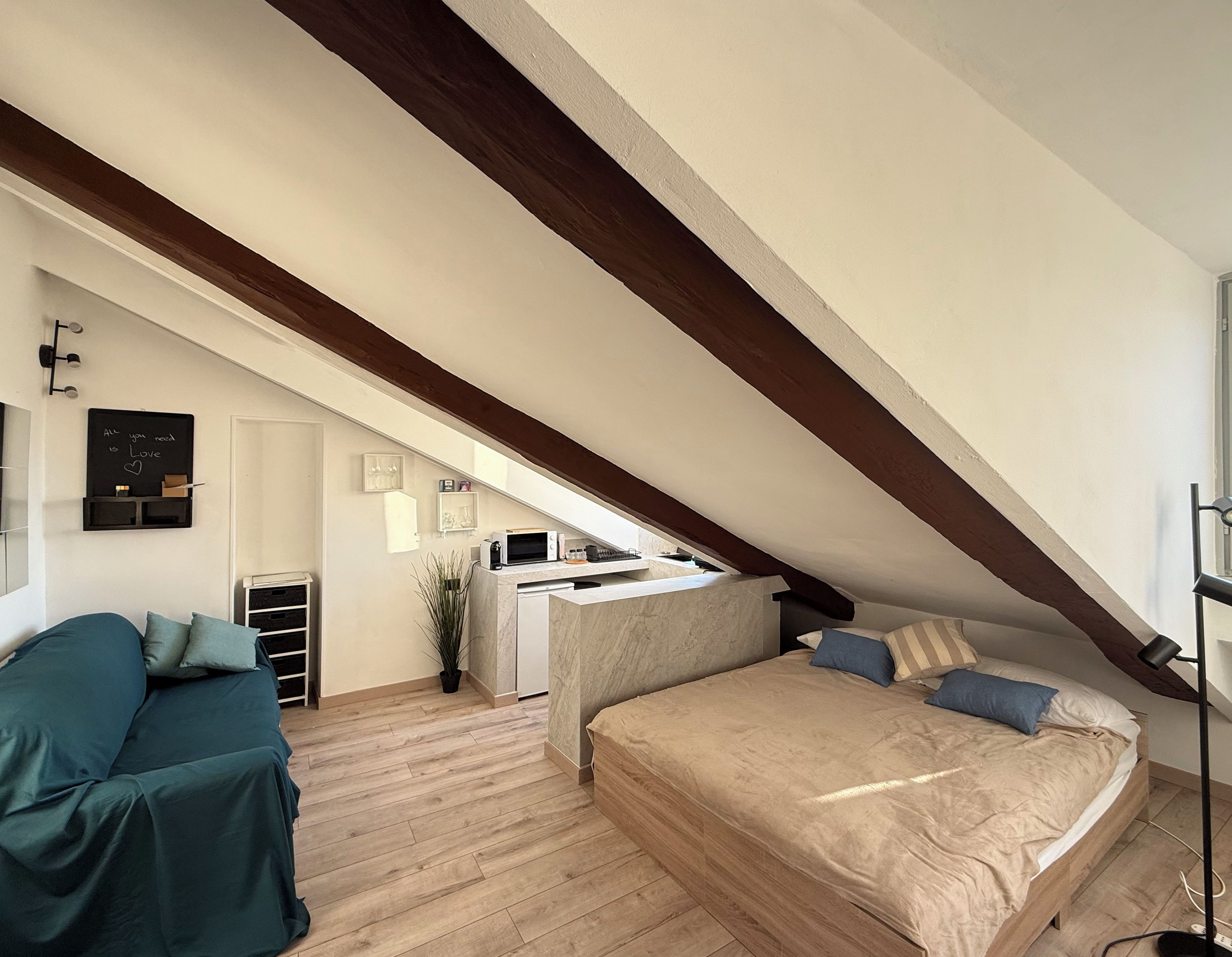 Un dormitorio con techo inclinado, una cama, un escritorio y una kitchenette.