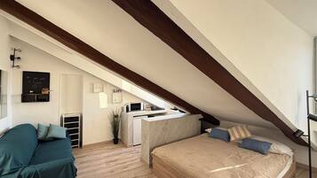 Un dormitorio con techo inclinado, una cama, un escritorio y una kitchenette.