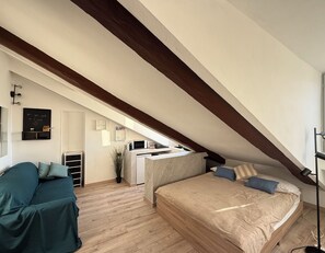 A bedroom with a sloped ceiling, a bed, a desk, and a kitchenette. - Mole House (Torino)