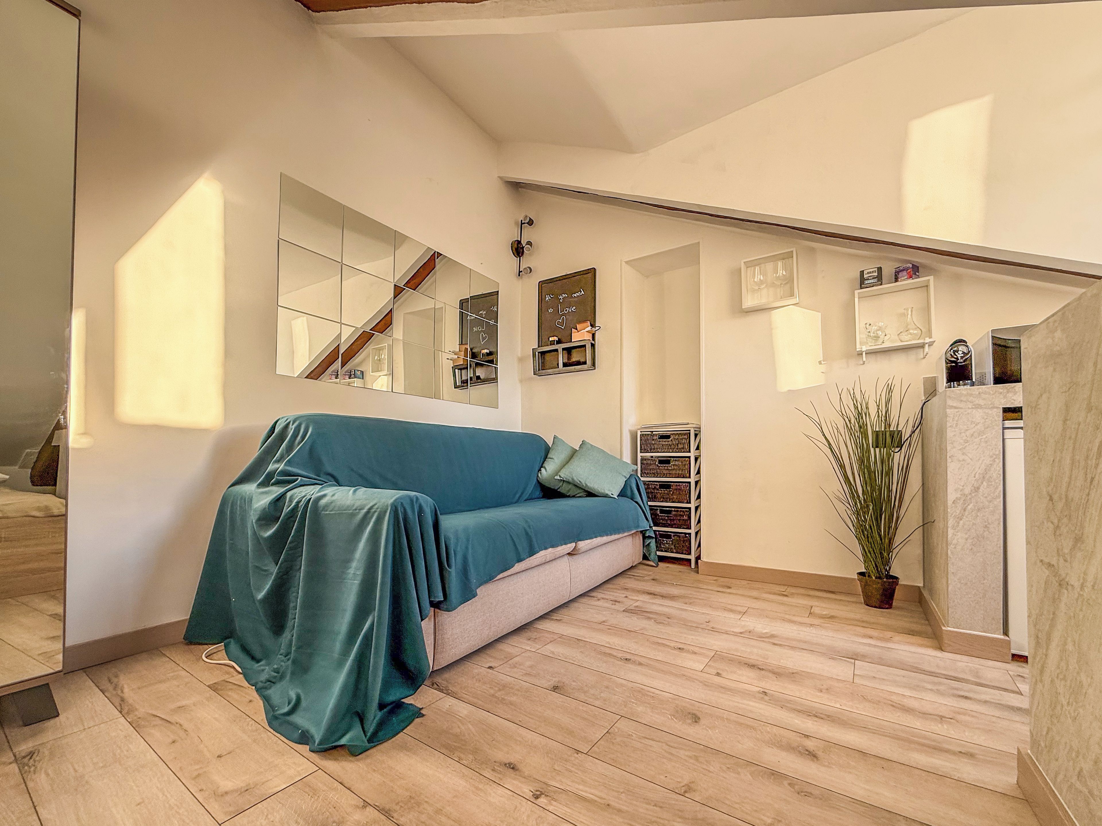 Una habitación con sofá tapizado, piso de madera, una escalera y una planta en maceta.