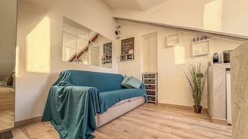 Una habitación con sofá tapizado, piso de madera, una escalera y una planta en maceta.