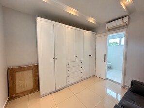 Una habitación con un armario blanco grande, un sofá gris y un ventanal corredera que da a un balcón.