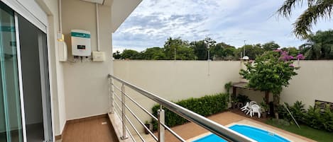 A balcony with a pool, a glass door, and a white wall with a water heater.
