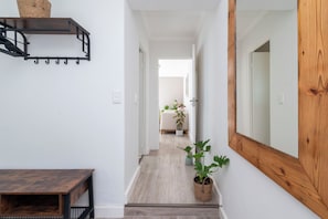 Un couloir avec un banc en bois, un miroir et une plante en pot.