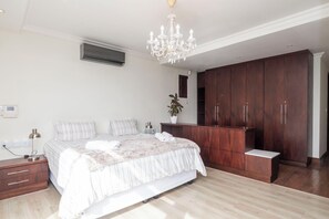 Une chambre à coucher comprenant un lit, une table de chevet, une lampe, un appareil de climatisation, une armoire et un lustre.