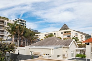 Un edificio residencial con techo plano, rodeado de palmeras y una montaña al fondo.
