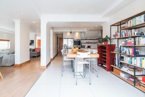 A modern kitchen with a dining area, a bookshelf, and a living room with a sofa. - 5BR Sea Point Oasis: Main House + Flatlet - Solar Powered - Heated Pool & Garage (Cape Town)