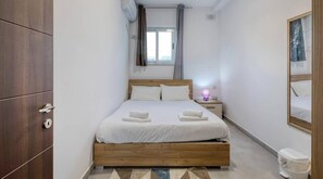 A bedroom with a wooden bed, a nightstand with a lamp, a window with curtains, and a mirror on the wall. - 2BR Penthouse, Private Rooftop Pool & Views - WIFI (Żurrieq)