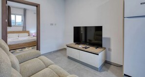 A modern hotel room with a bed, a television on a stand, and a refrigerator. - 2BR Penthouse, Private Rooftop Pool & Views - WIFI (Żurrieq)