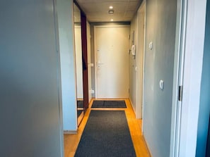 Un couloir étroit, dont le sol est recouvert d’une moquette, mène à une porte.