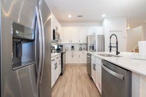 Une cuisine moderne dotée d’appareils électroménagers en acier inoxydable, de meubles blancs et d’un plancher en bois.
