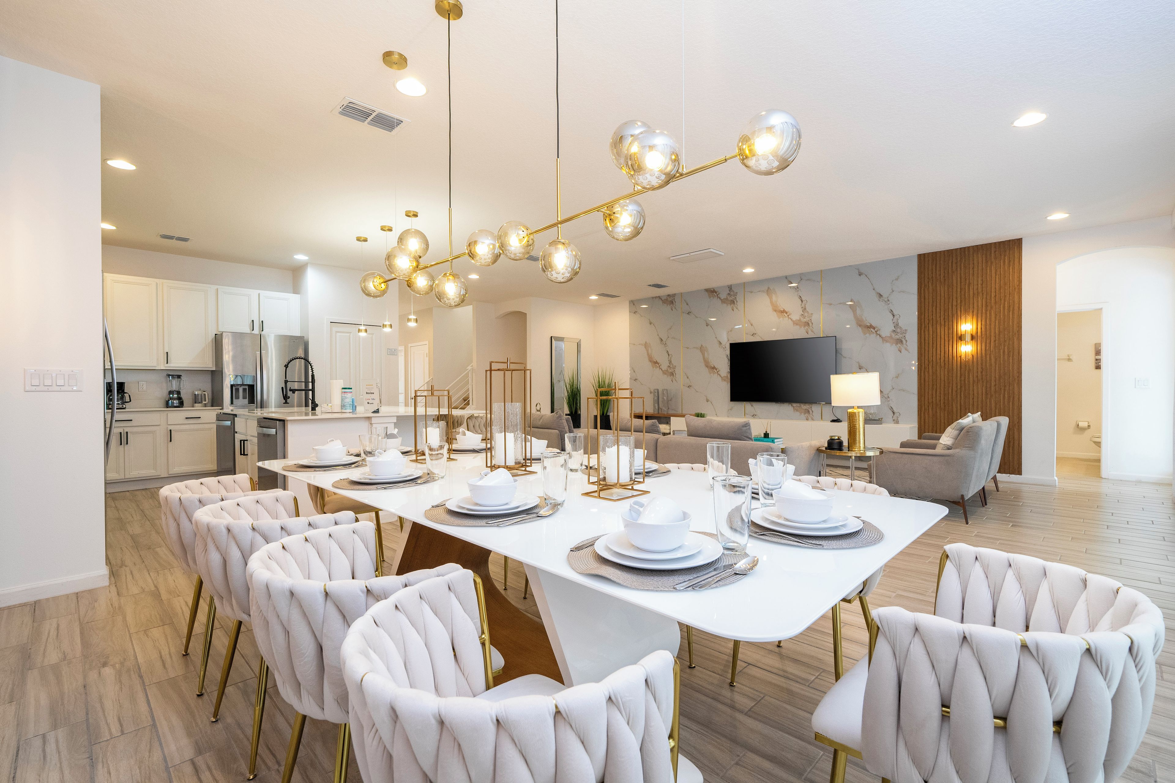 A modern dining area with a white table set for six, surrounded by plush chairs, and a kitchen in the background.
