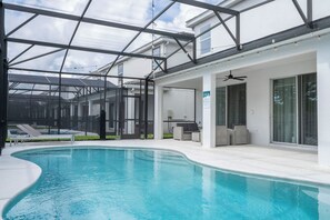 Ein Schwimmbad mit Glasüberdachung, Liegestühlen und Deckenventilator.