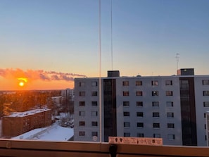 Un edificio de gran altura con múltiples ventanas, cielo despejado y un atardecer al fondo.