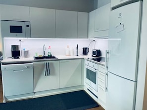 Una cocina moderna con armarios blancos, lavavajillas, cafetera y refrigerador.