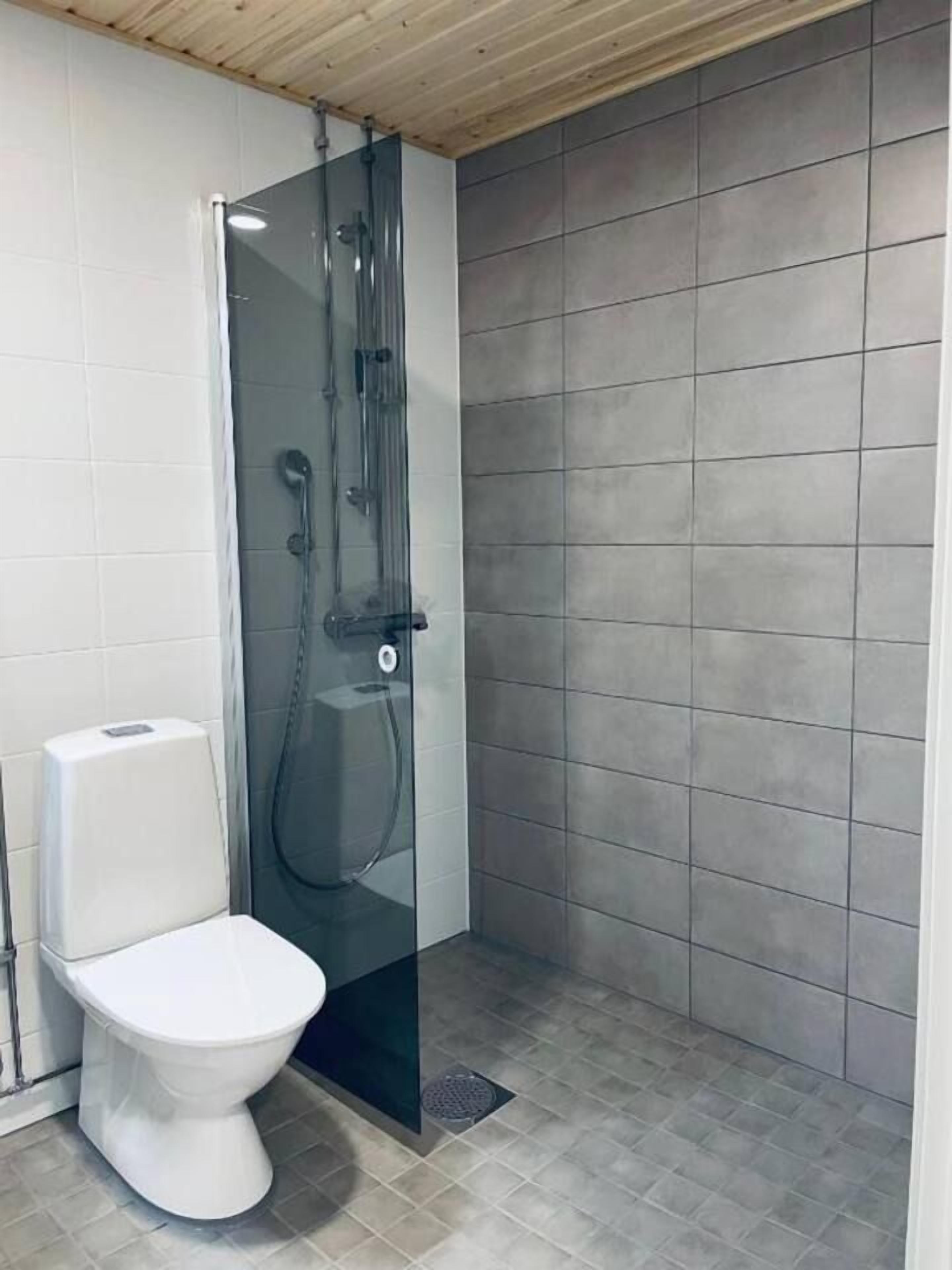Ein Badezimmer mit einer Duschkabine, einer weißen Toilette und grauen Fliesenwänden.