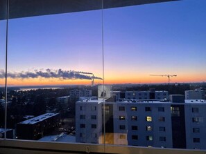 Une vue à travers une fenêtre, donnant sur un paysage urbain au crépuscule, avec des bâtiments modernes et un ciel dégagé.