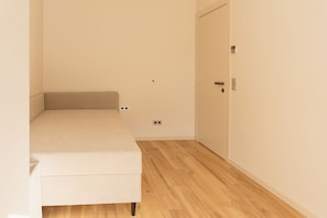 A small, unadorned room with a single bed, a door, and a light switch on the wall. - Fischer's Apartment 1: New construction, first-time occupancy, modern and stylish, quiet, parking space, terrace (Starnberg)