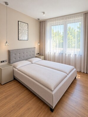 A modern bedroom with a large bed, bedside tables, a hanging light fixture, and a window with sheer curtains. - Fischer's Apartment 1: New Construction, First Occupancy, 2 Bedrooms, Parking, Terrace, Lake 1 km Away (Starnberg)