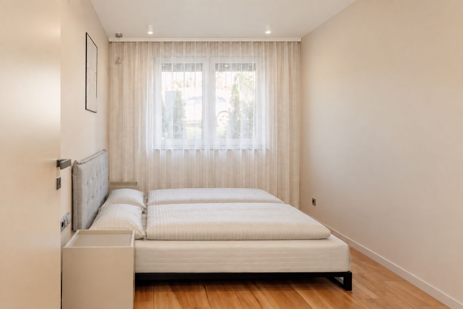 A bedroom with a bed, a bedside table, a window with curtains, and a picture on the wall.