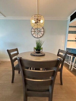 Een eetruimte met een ronde tafel, vier stoelen, een hanglamp en een wandklok.