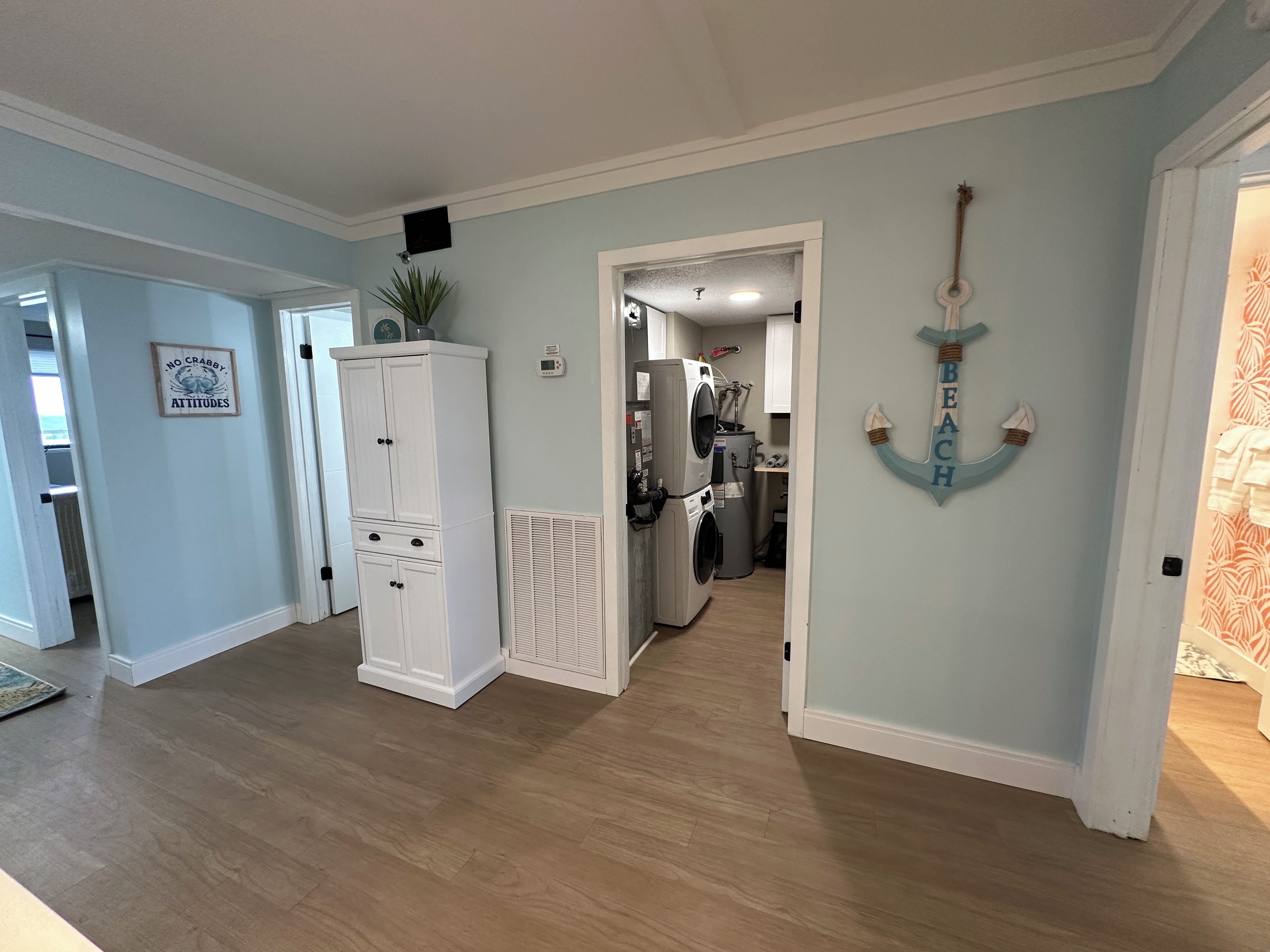 A hallway with a white cabinet, a wall-mounted air vent, and a door leading to a kitchen area with a refrigerator and washing machine.