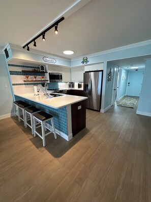 Cozinha moderna com ilha central, eletrodomésticos de aço inoxidável e painel de proteção azul.