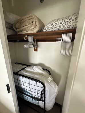 Uma cama de solteiro com prateleira de madeira acima e suporte de metal abaixo.