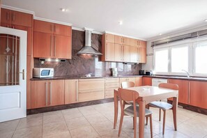 A modern kitchen with wooden cabinets, a built-in microwave, and a dining area with a table and chairs. - Villa Mahon - Six Bedroom Villa, Sleeps 12 (Javea)