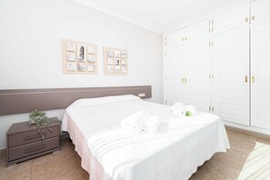 Een hotelkamer met een bed, nachtkastje, kledingkast en ingelijste foto’s aan de muur.