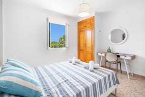 Ein Schlafzimmer mit Bett, Schreibtisch, Stuhl, Fenster und Tür.