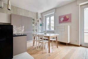 A modern kitchen with a dining area, wooden flooring, and a large window providing natural light. - Hostmate - Milano - C. Buenos Aires - City Center (Milan)