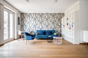 Ein modernes Wohnzimmer mit einer Wand im geometrischen Muster, einem blauen Sofa und einer weißen Schrankwand.