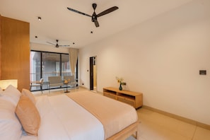 A modern hotel room with a large bed, a ceiling fan, a seating area with a table and chairs, and a view through a large window.