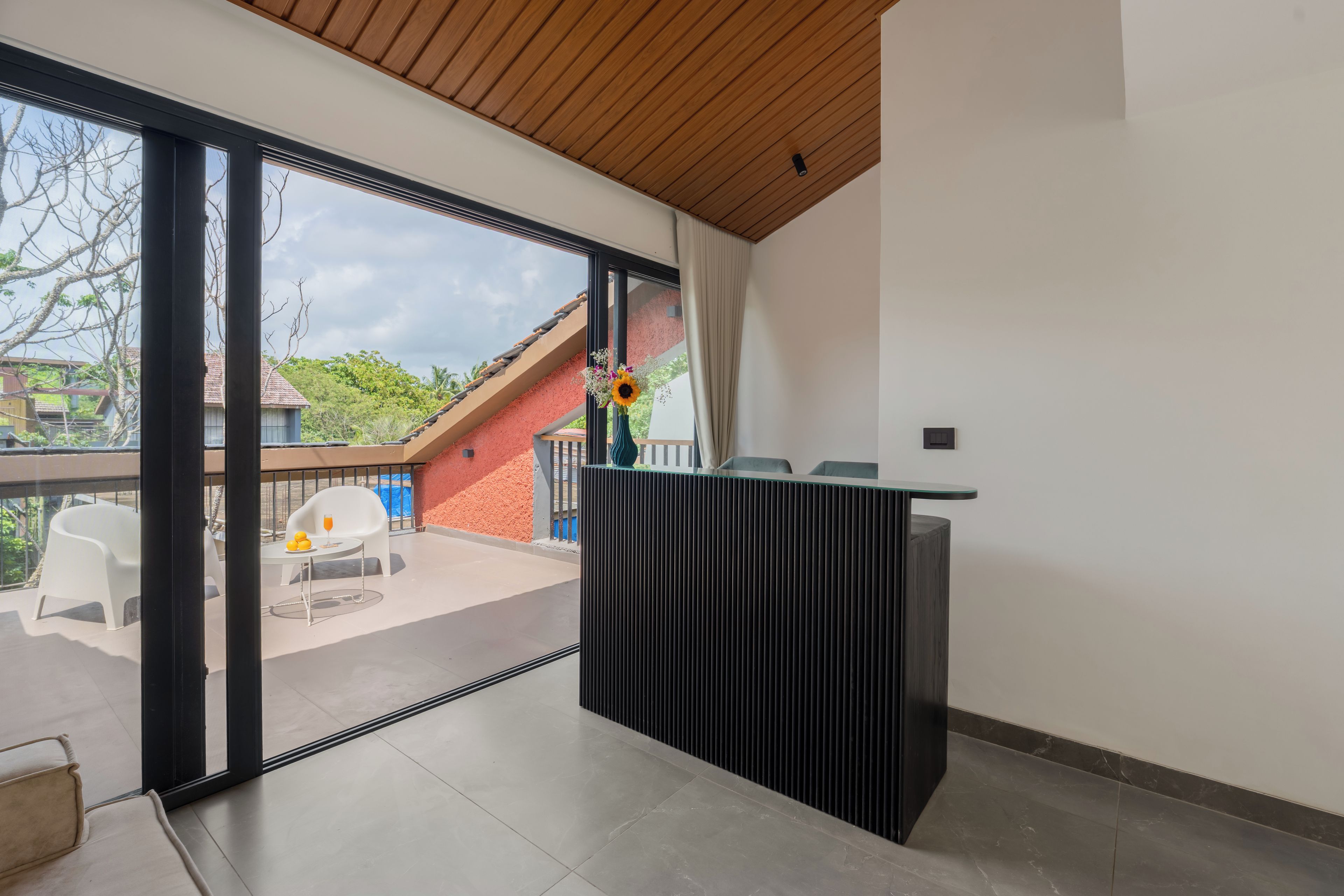 A modern interior with a large sliding glass door leading to an outdoor area, a small table with a glass of orange juice, and a decorative vase with flowers.