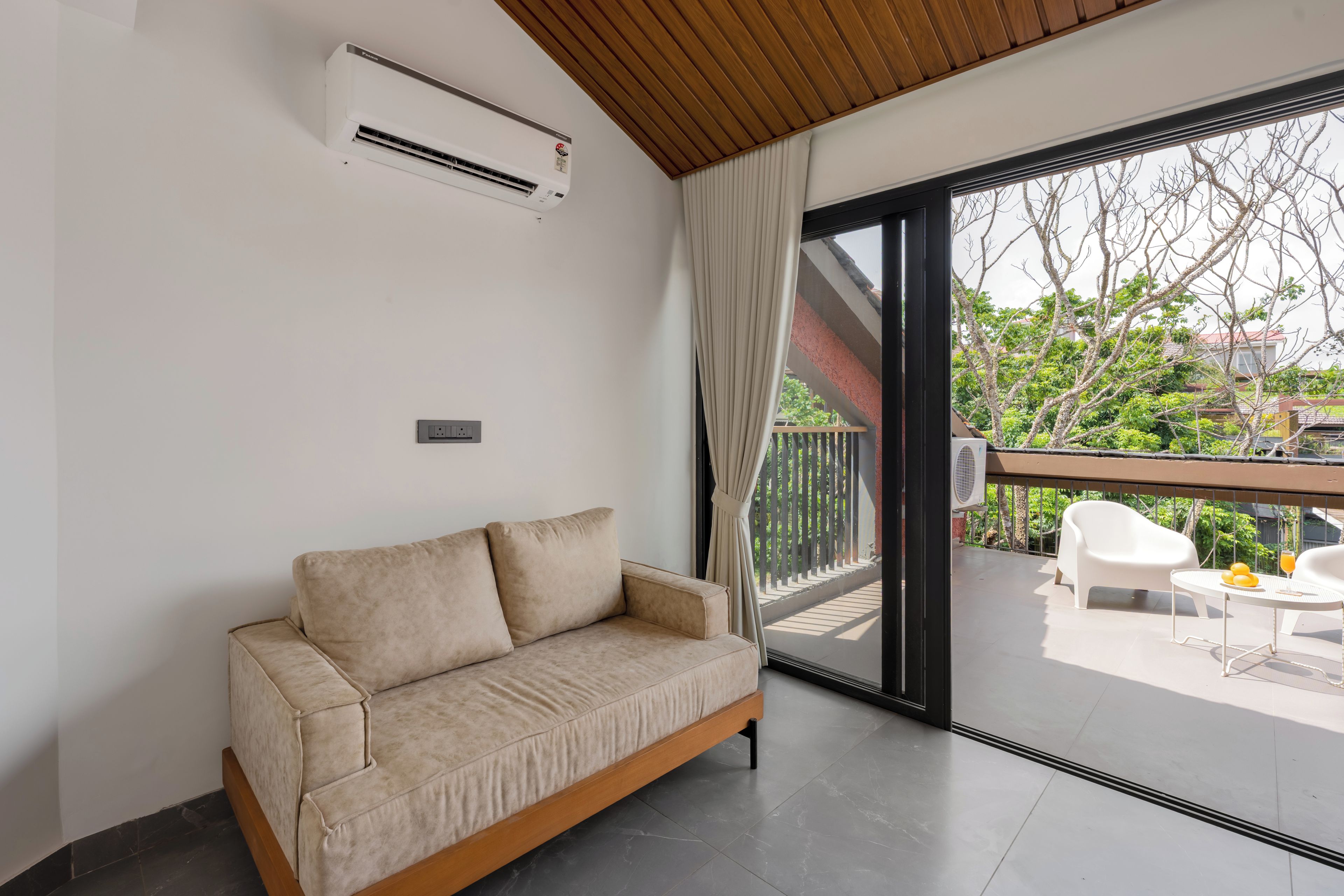 A modern living room with a sofa, a ceiling-mounted air conditioner, and a large sliding glass door leading to an outdoor balcony.