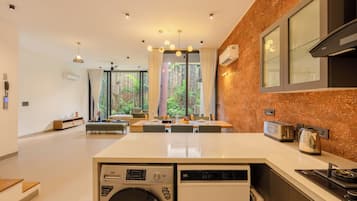 A modern kitchen with a built-in washer and dryer, a dining area with a view of the garden, and a large window with curtains.