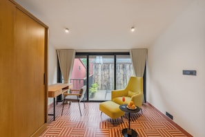 A modern room with a wooden wardrobe, a desk, a yellow armchair, and a view of a red building through a glass door. - ELIVAAS Signature Coco Baia 3BHK Villa (Marra)
