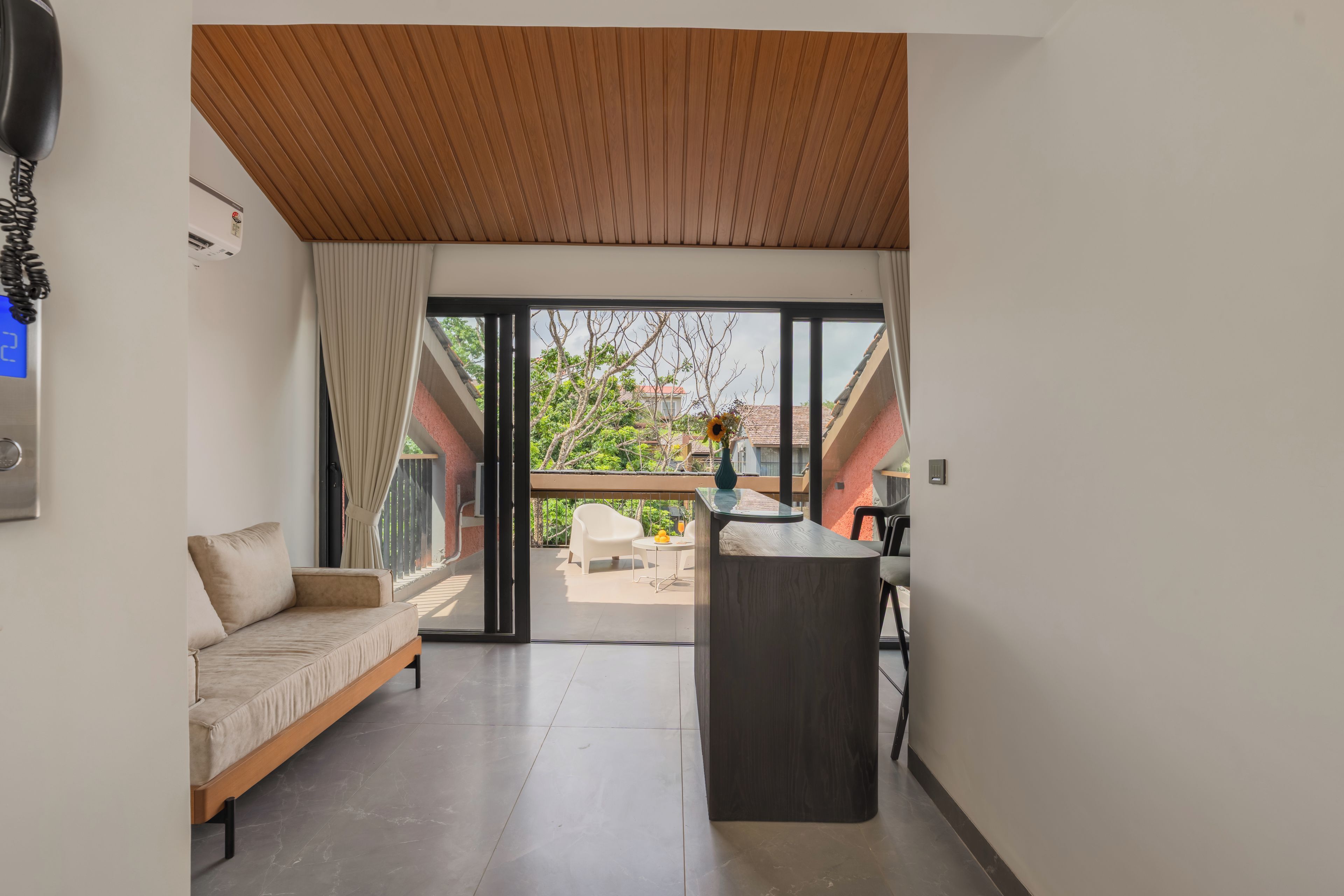 A modern interior with a sofa, a small table, and a view of a garden through a glass door.