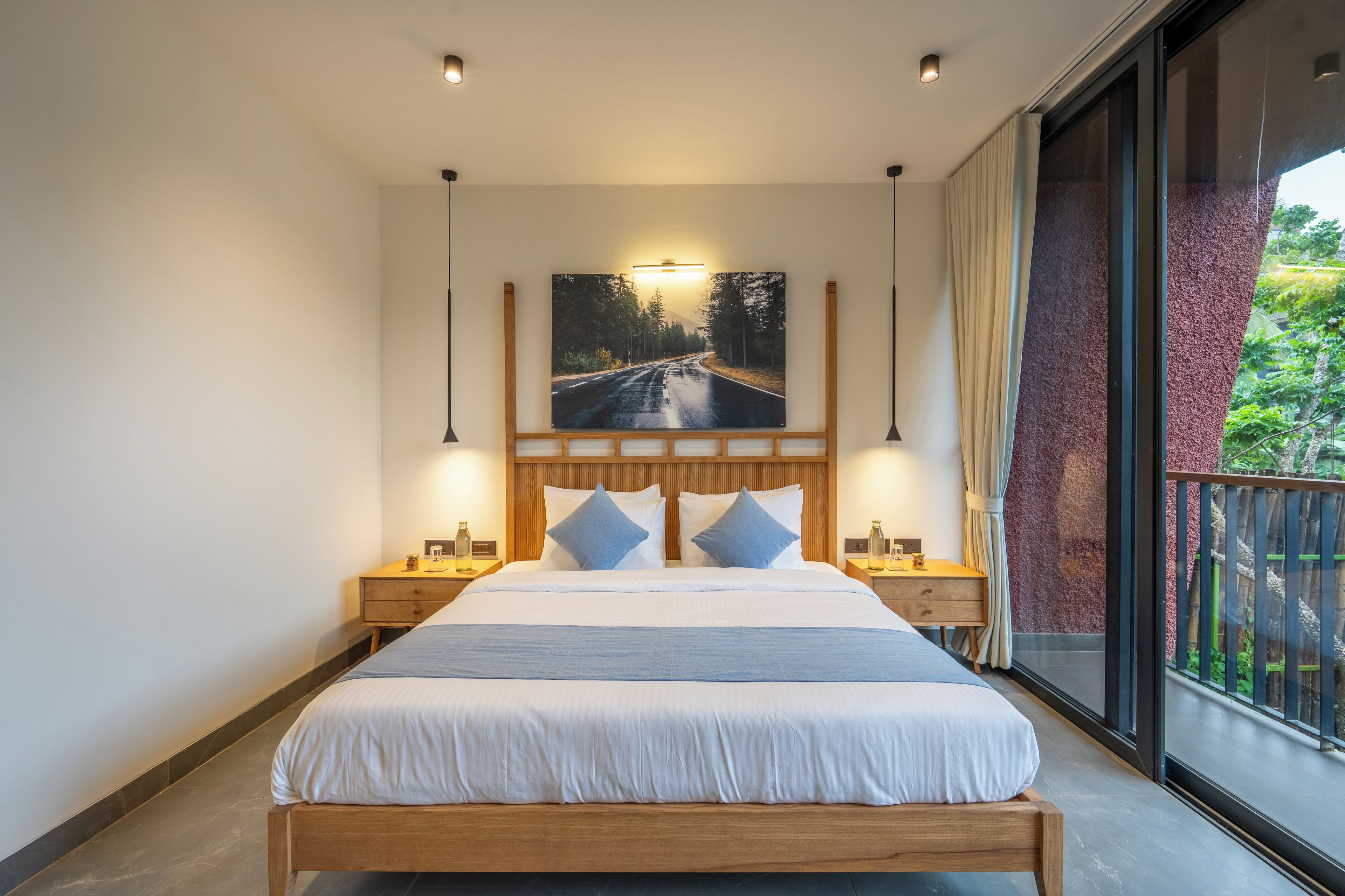 A modern bedroom with a large bed, wooden headboard, two bedside tables, and a large window with a view of greenery.