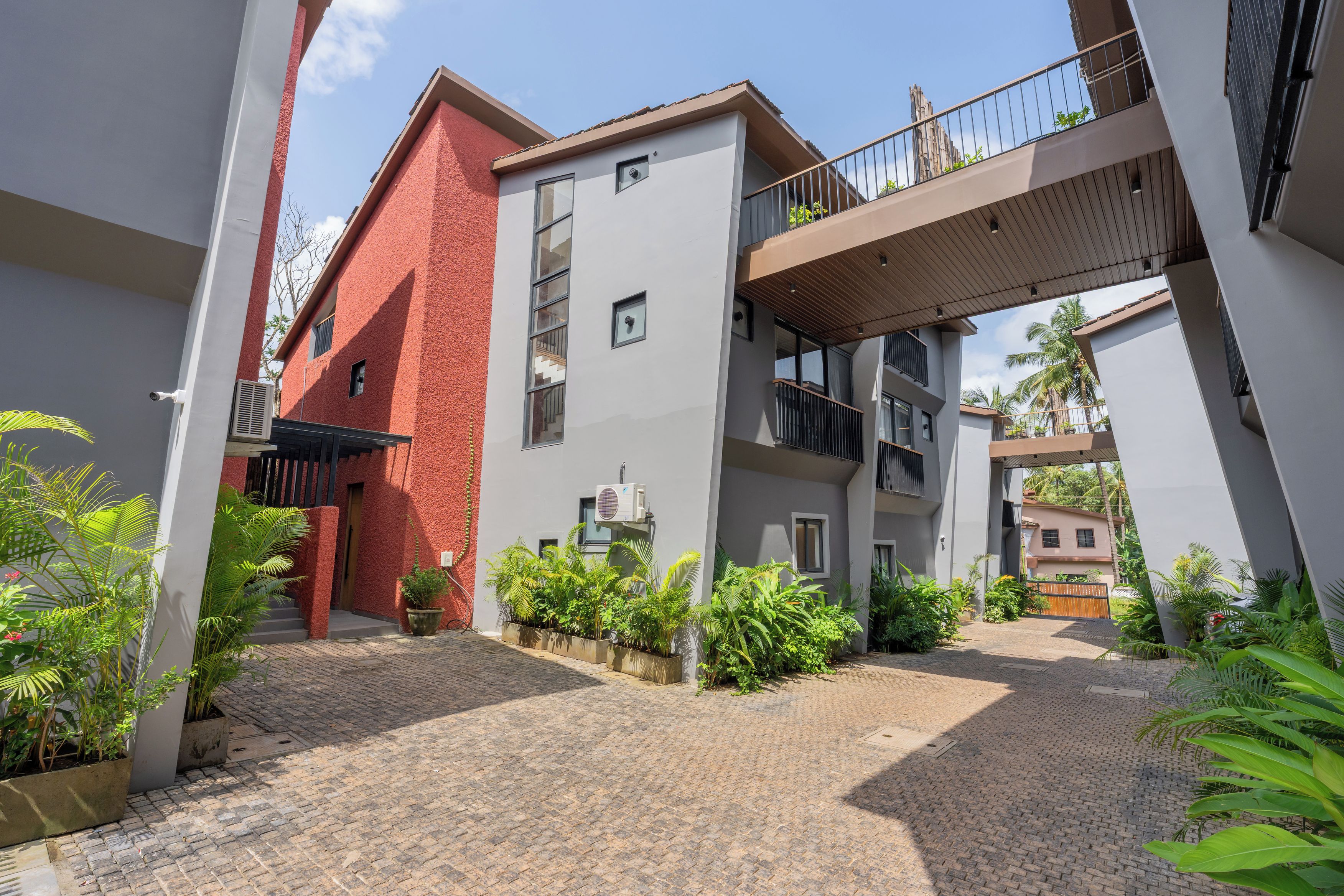 A courtyard with a red brick building, a grey building with a balcony, and potted plants.