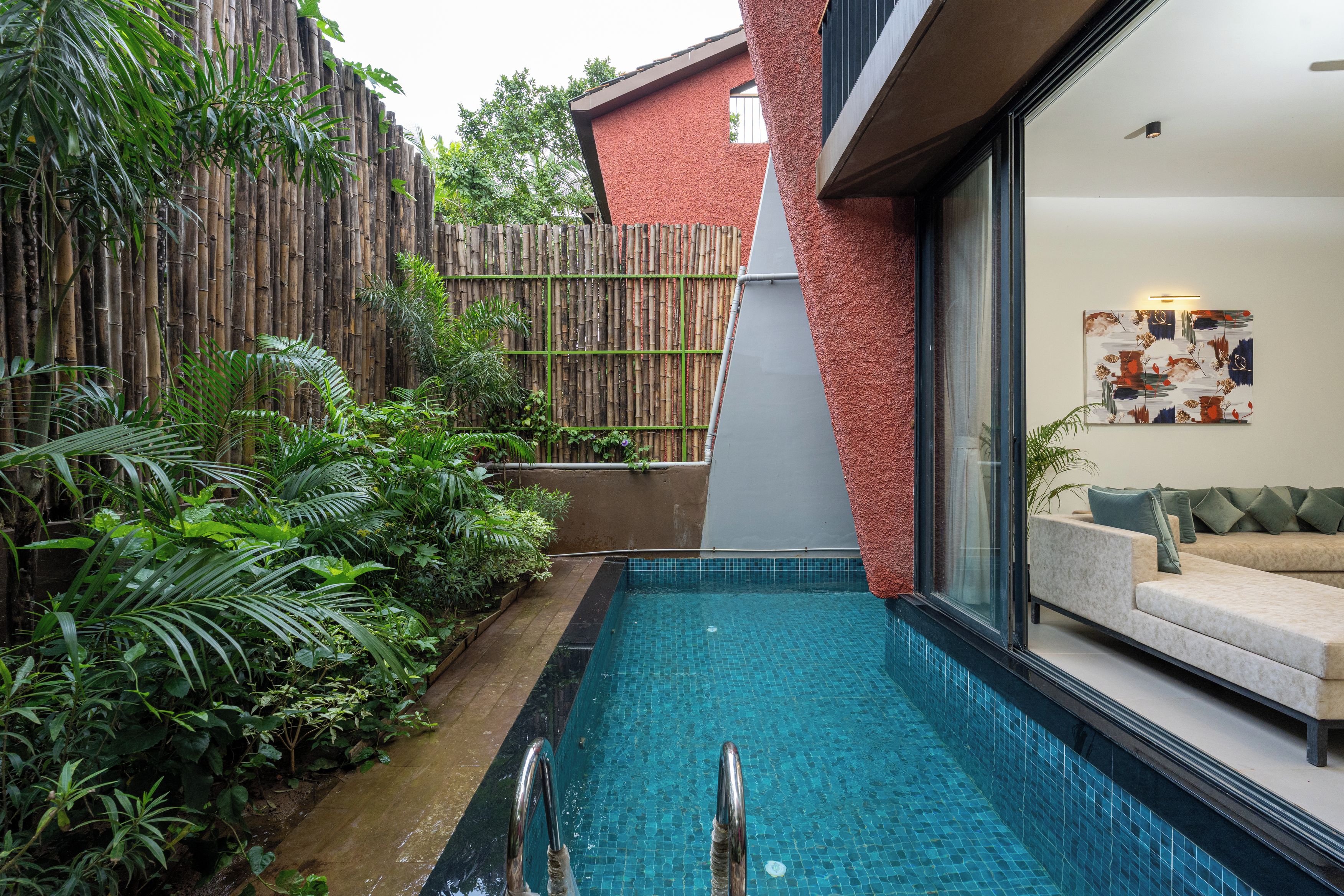 A modern pool with a glass wall, surrounded by lush greenery and a bamboo fence.