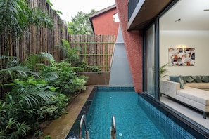 A modern pool with a glass wall, surrounded by lush greenery and a bamboo fence.