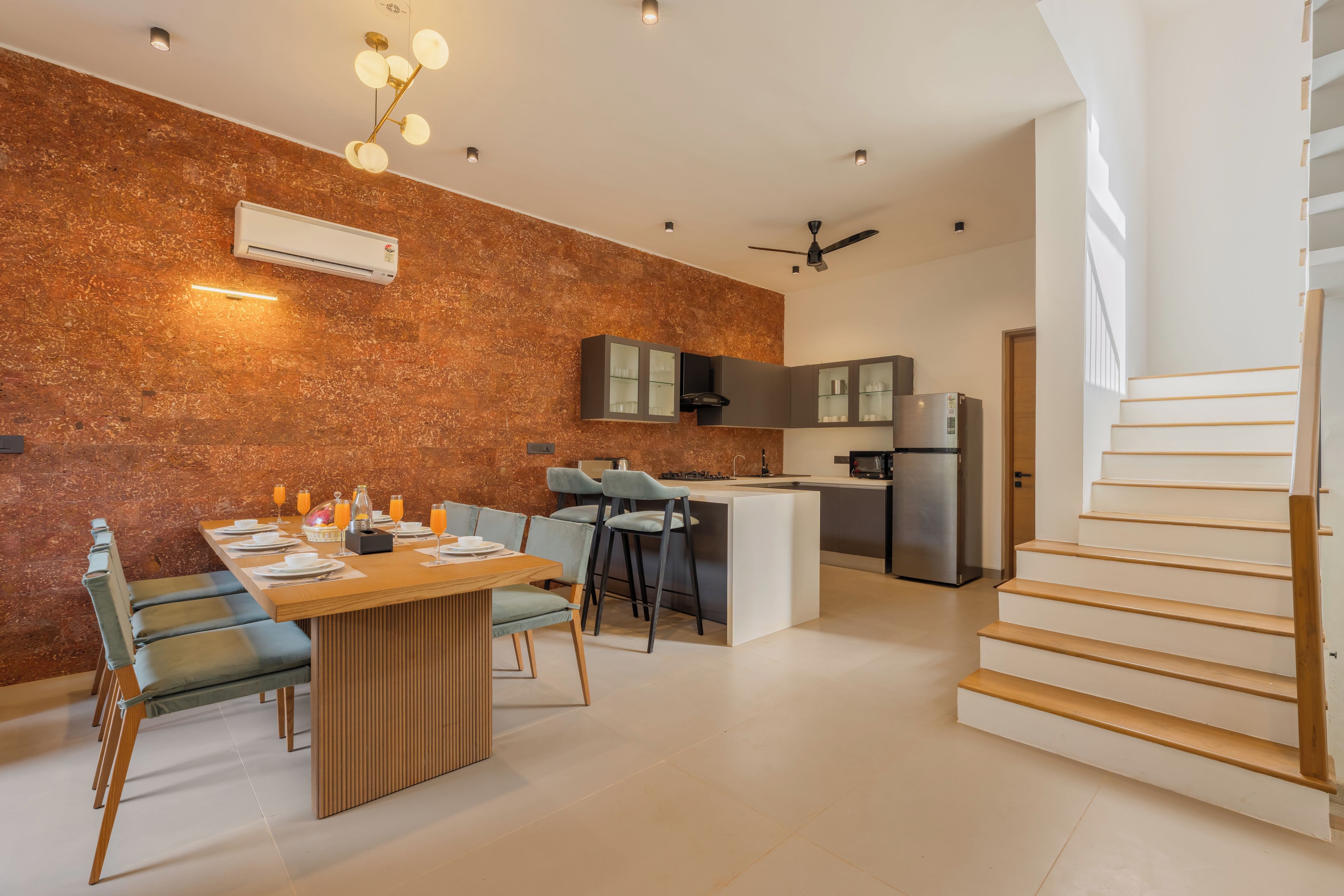 A modern kitchen with a built-in island, a dining area with a wooden table and chairs, and a staircase leading to an upper level.