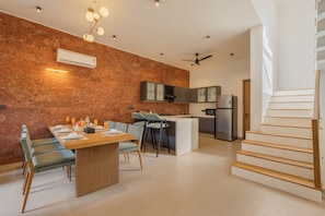 A modern kitchen with a built-in island, a dining area with a wooden table and chairs, and a staircase leading to an upper level.
